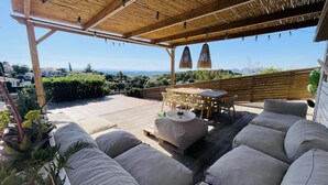 Een terras buiten met een houten pergola, zithoek en een tafel.