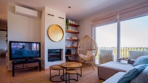 Een moderne woonkamer met een flatscreen-tv, een bank, een rieten fauteuil, een ronde wanddecoratie en een raam met uitzicht.