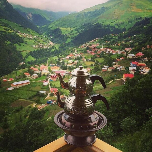 A view of a village from a high vantage point, with a traditional metal teapot in the foreground.