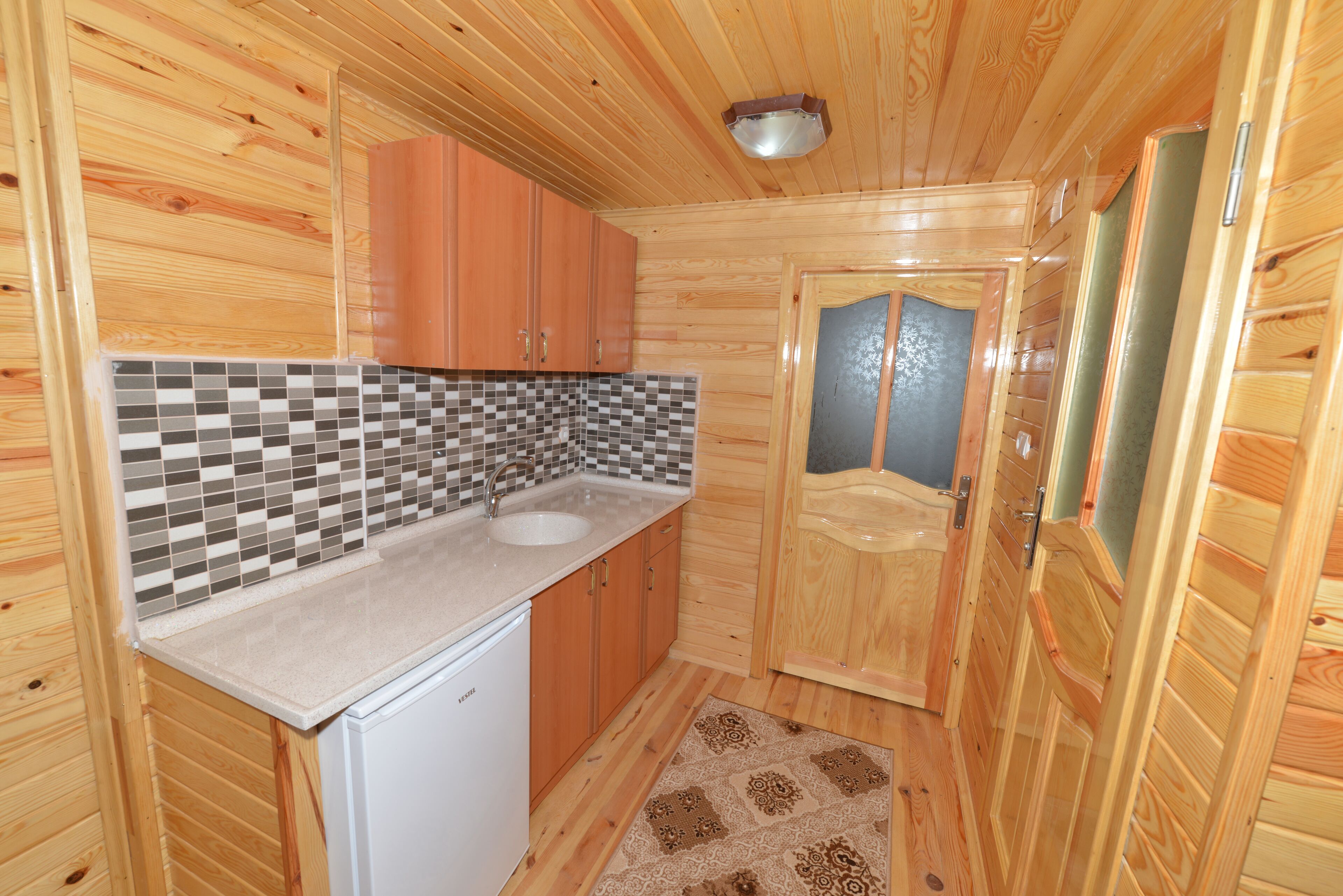 Cocina compacta con armarios de madera, salpicadero de azulejos y lavamanos integrado.