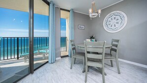A balcony with a view of the ocean, a dining table with chairs, a chandelier, and a decorative plate on the wall. - Vacations are BETTER on the BEACH! ** 1BR @ Phoenix V (Orange Beach)