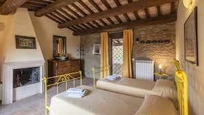 A bedroom with two beds, a stone wall, a fireplace, and a rustic wooden ceiling.