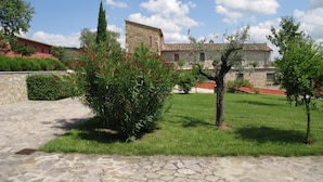 A stone courtyard with a stone building in the background, surrounded by green grass and trees.