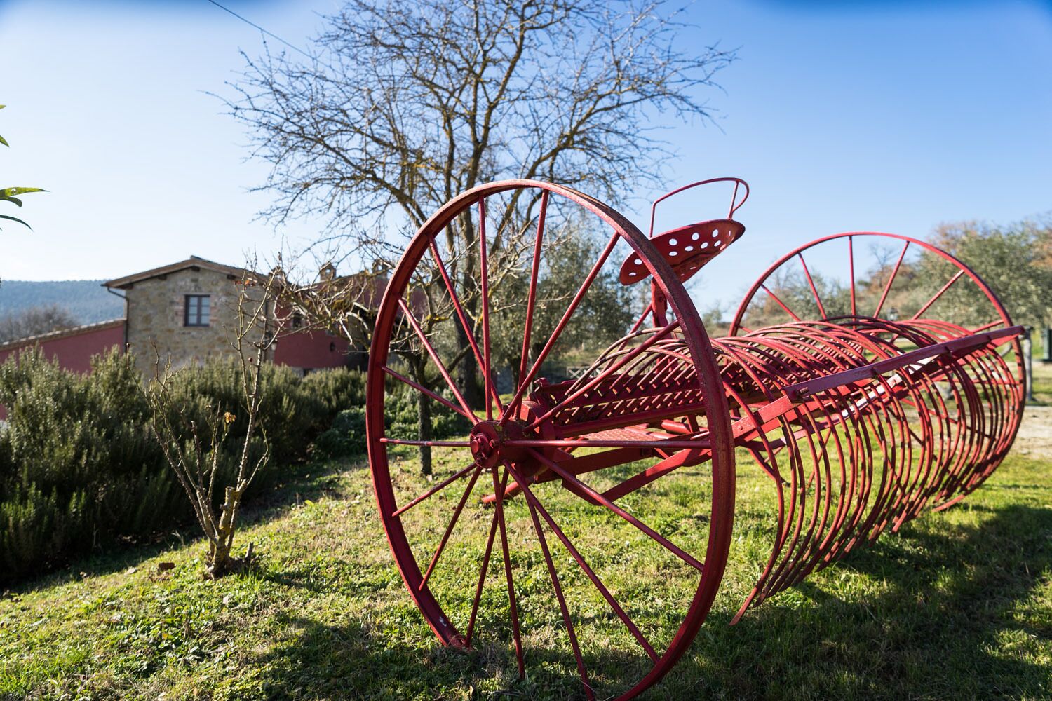 Una escultura metálica roja en un área verde, con un edificio de piedra al fondo.