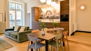 Una sala de estar moderna con sofá, mesa de comedor, sillas y una cocina con mural y lámparas colgantes.