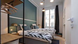 Un dormitorio moderno con cama, mesitas de noche, lámpara y ventana con cortinas.