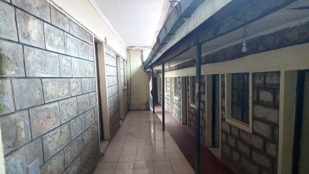 Un couloir au sol carrelé, aux murs en pierre et au plafond avec des poutres apparentes.
