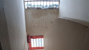 Un escalier étroit, dont les marches sont recouvertes de carreaux, mène à une fenêtre grillagée.