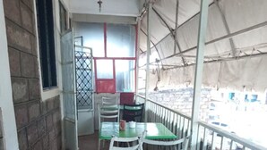 Un espace extérieur abrité, avec des tables et des chaises, donnant sur la rue, et un bâtiment doté d’une fenêtre et d’une porte.