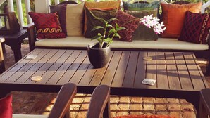 A wooden deck with a sofa and chairs, a table with a plant and coaster, and a brick wall in the background. - Captivating 3-bed Villa in Montego Bay (Montego Bay)