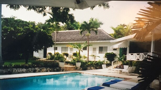 A swimming pool with lounge chairs, surrounded by greenery and a house with a sloped roof. - Captivating 3-bed Villa in Montego Bay (Montego Bay)