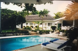 A swimming pool with lounge chairs, surrounded by greenery and a house with a sloped roof. - Captivating 3-bed Villa in Montego Bay (Montego Bay)