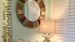 Un meuble en bois rustique, surmonté d’un miroir, orné d’une étoile de mer et sur lequel est posée une lampe.
