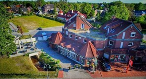 Un grand bâtiment à plusieurs étages, doté d’un toit rouge bien visible, d’un espace extérieur couvert avec des sièges et d’une enseigne indiquant qu’il s’agit d’un hôtel.