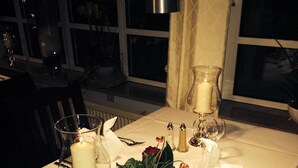 Et bord dækket til to med hvid dug, stearinlys, en blomstervase og salt- og peberkværke.