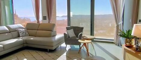 A modern living room with a large sofa, a patterned armchair, a small round table, and a potted plant.