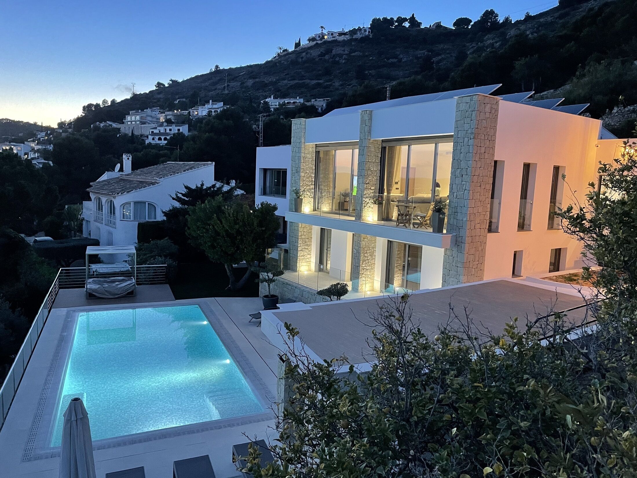 Une maison moderne à deux étages, dotée d’une piscine, d’une façade en pierre et de grandes fenêtres.