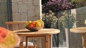 A wooden table with a bowl of fruit, a stone wall, and a glass railing with flowers. - House - Sleeps 8 - Pool - Garden - Parking (Javea)