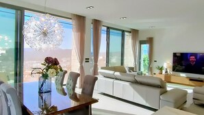 A modern living room with a glass dining table, white sofas, and a large TV. - House - Sleeps 8 - Pool - Garden - Parking (Javea)