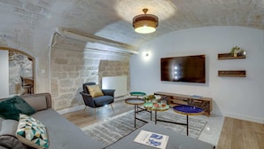 A cozy living room with a stone wall, a comfortable sofa, a modern armchair, a coffee table, and a flat-screen TV mounted on the wall. - Sweett | Trevise - Three Bedroom Apartment, Sleeps 6 (Paris)