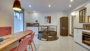 A modern kitchen with a central island, a dining area with a wooden table and pink chairs, and a refrigerator. - Sweett | Trevise - Three Bedroom Apartment, Sleeps 6 (Paris)