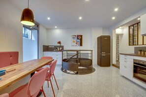 Una cocina moderna con una isla central, un comedor con mesa de madera y sillas rosas, y un refrigerador.