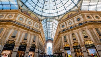 A grand, ornate building with a glass dome ceiling and multiple storefronts, including Prada and Versace.