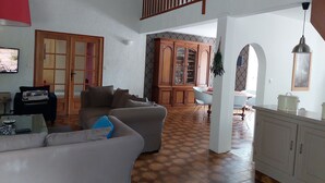 A spacious living area with a high ceiling, a wooden staircase, a dining area, and a kitchen with white cabinets.