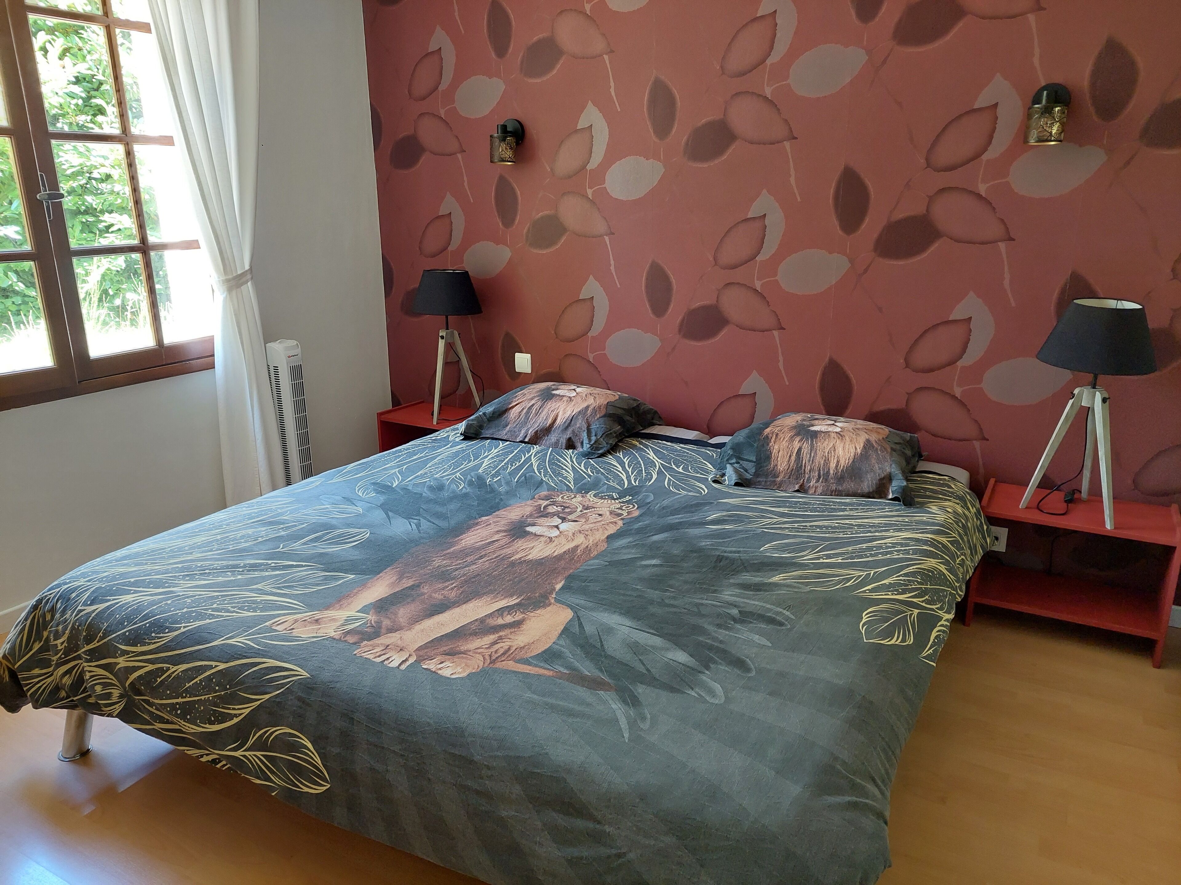 A bedroom with a bed, two bedside tables with lamps, a window with curtains, and a radiator.