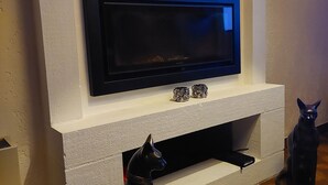 A modern living room with a flat-screen TV mounted on a white wall, a decorative clock, and a black cat statue.