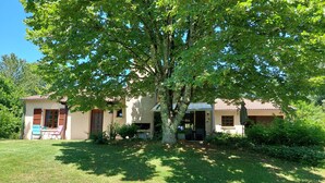 A two-story house with a patio area, a tree in front, and a lawn.