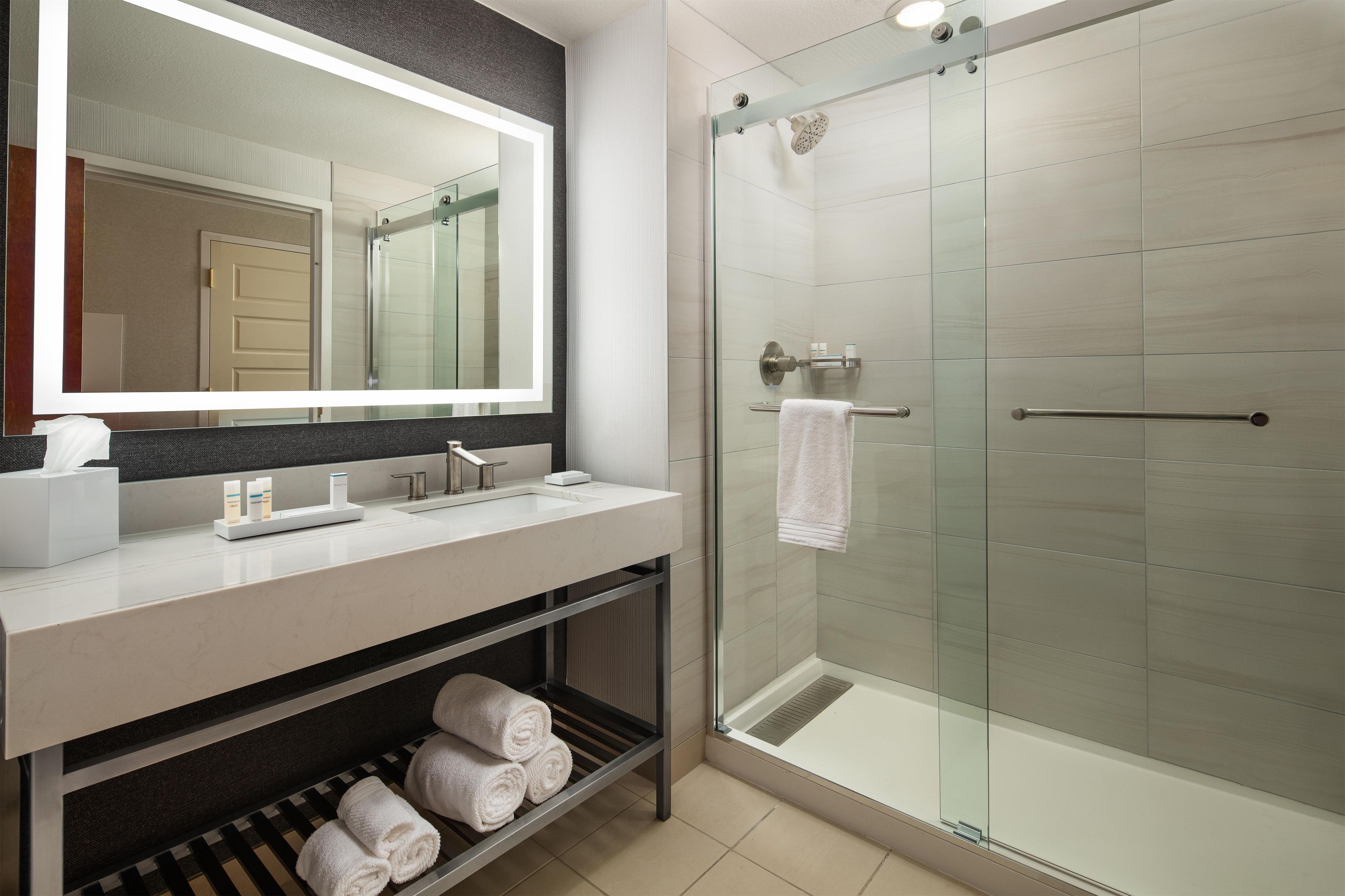 Un baño moderno con cabina de ducha de vidrio, tocador con espejo y toallero.