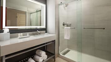 Un baño moderno con cabina de ducha de vidrio, tocador con espejo y toallero.