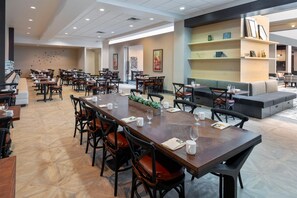 Un comedor amplio con varias mesas y sillas, una zona de estar con sofás y una pared con estanterías que exhiben objetos decorativos.