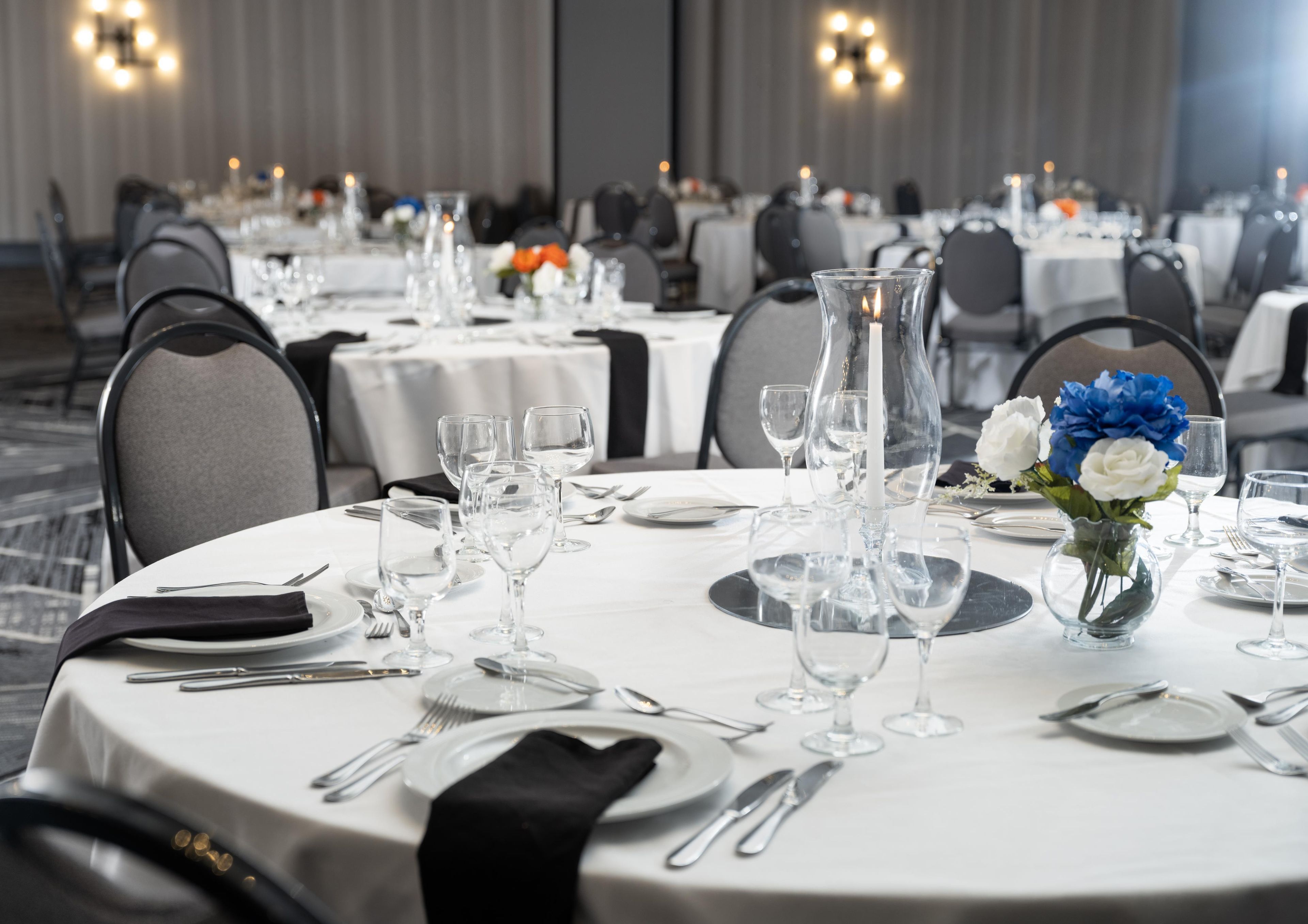 A banquet hall with round tables set for dining, featuring clear glassware, plates, and cutlery.
