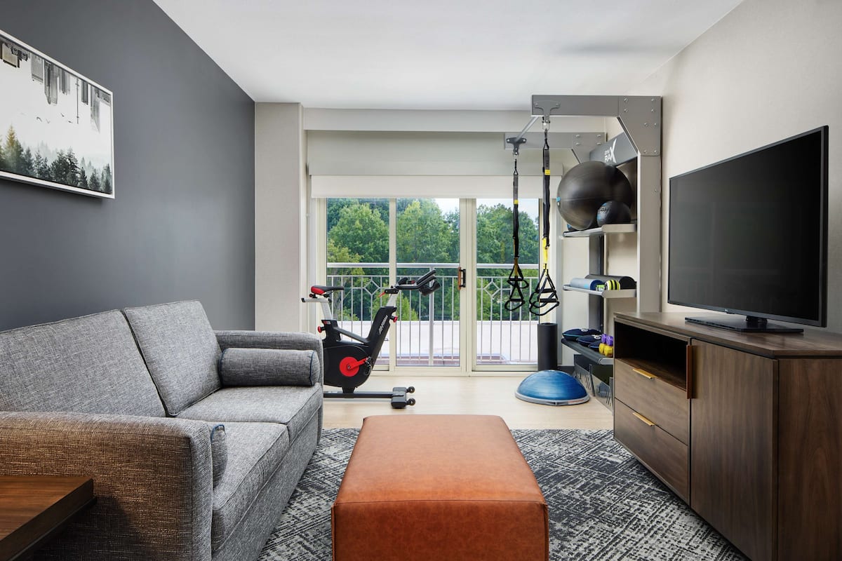 Una sala moderna con un sofá gris, un mueble de madera, un televisor de pantalla plana y equipo de ejercicio.