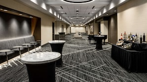 Ein Hotelkorridor mit einer langen Reihe runder Tische, einer Sofaecke und einer Bar mit Flaschen und Gläsern.