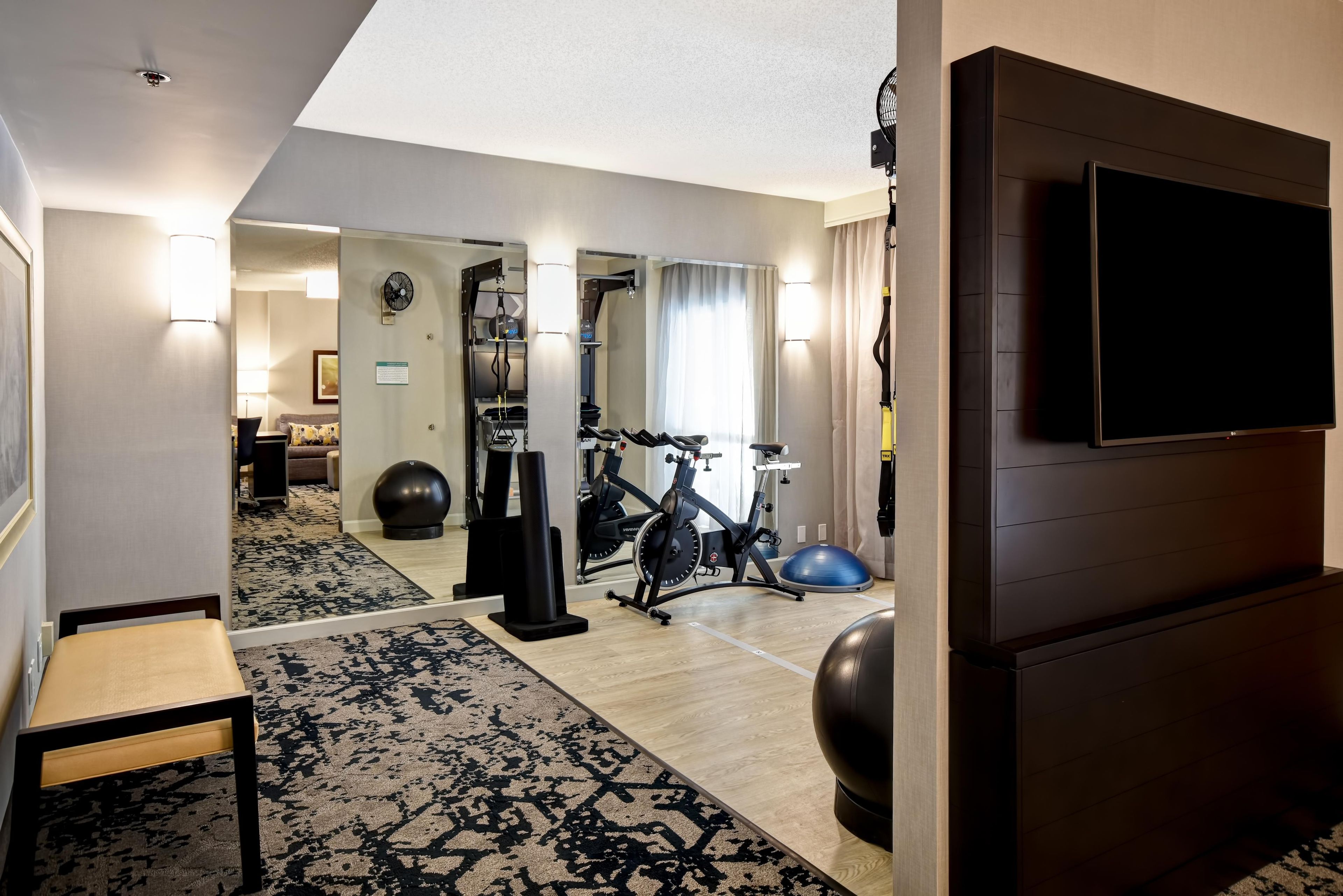 A hotel room with a treadmill, exercise ball, and a television.