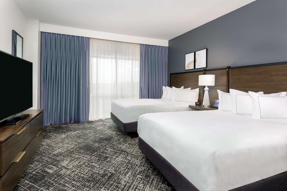 Une chambre d’hôtel avec deux lits, une télévision, un bureau et une fenêtre avec des rideaux.