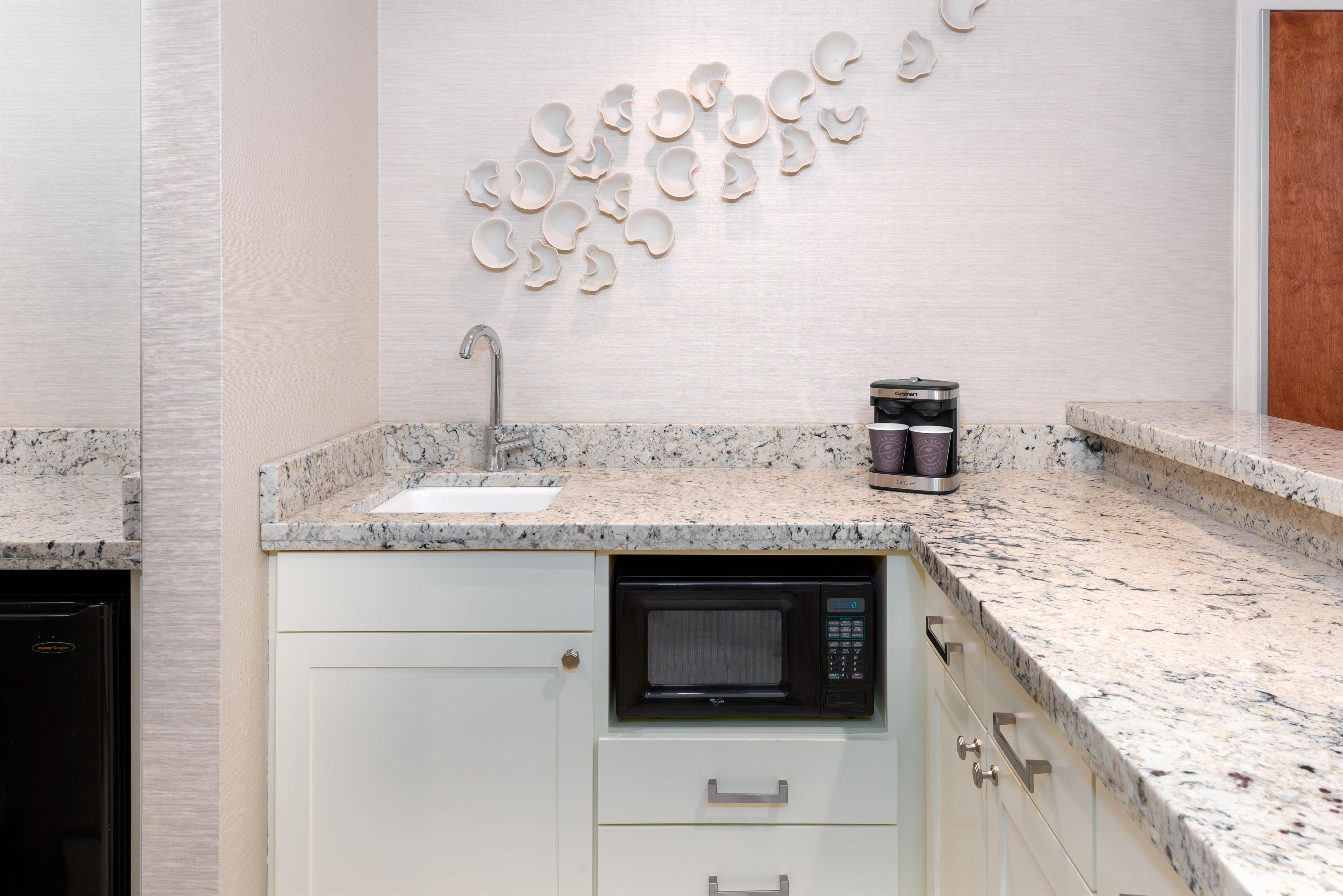 A kitchen with a granite countertop, a built-in microwave, a coffee maker, and a wall-mounted sink.