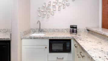 A kitchen with a granite countertop, a built-in microwave, a coffee maker, and a wall-mounted sink.
