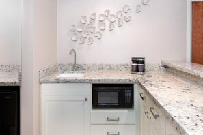 A kitchen with a granite countertop, a built-in microwave, a coffee maker, and a wall-mounted sink. - Hilton Charlotte Airport (Charlotte)