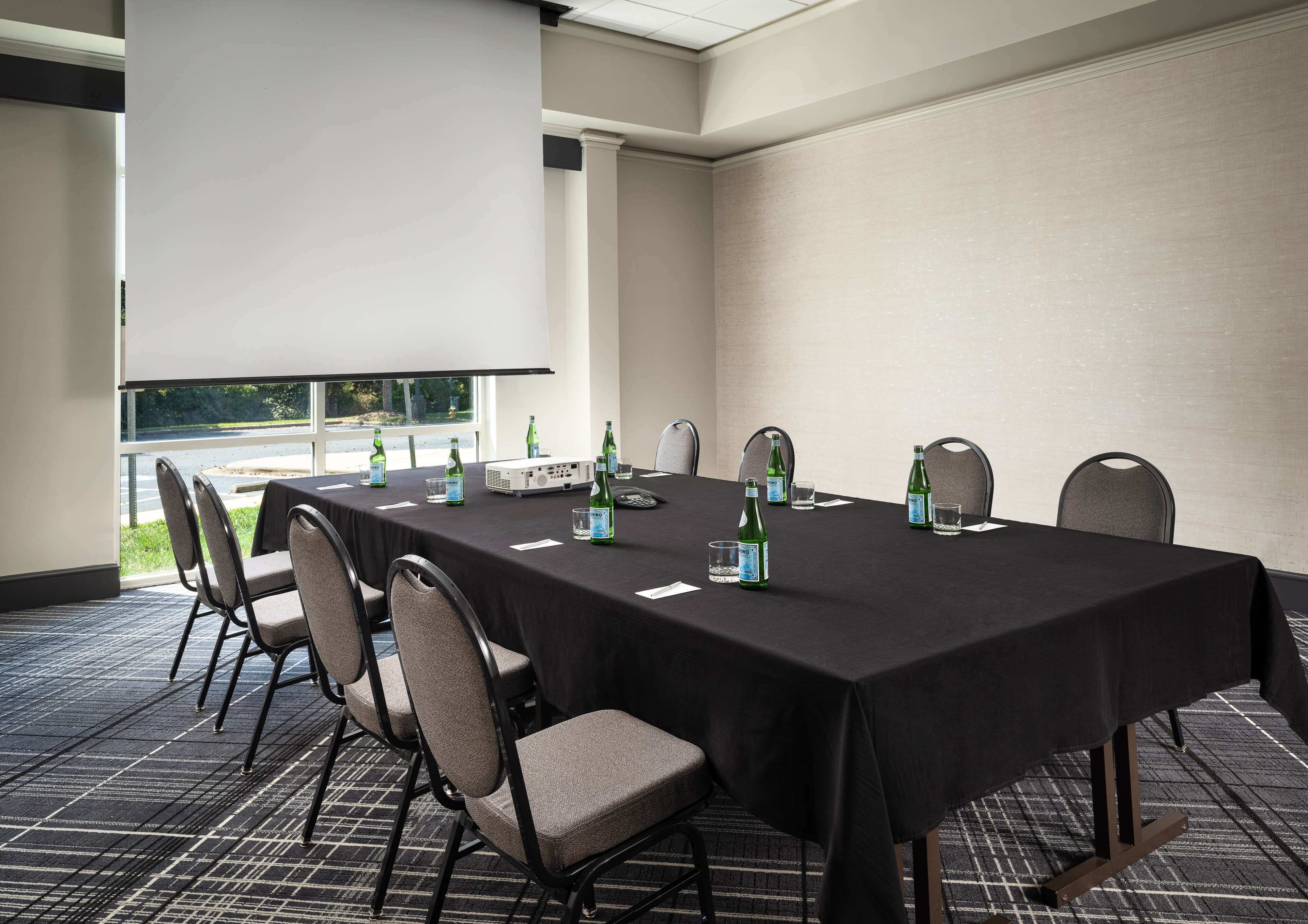 Un salón de conferencias con una larga mesa, sillas, un proyector y botellas de agua.