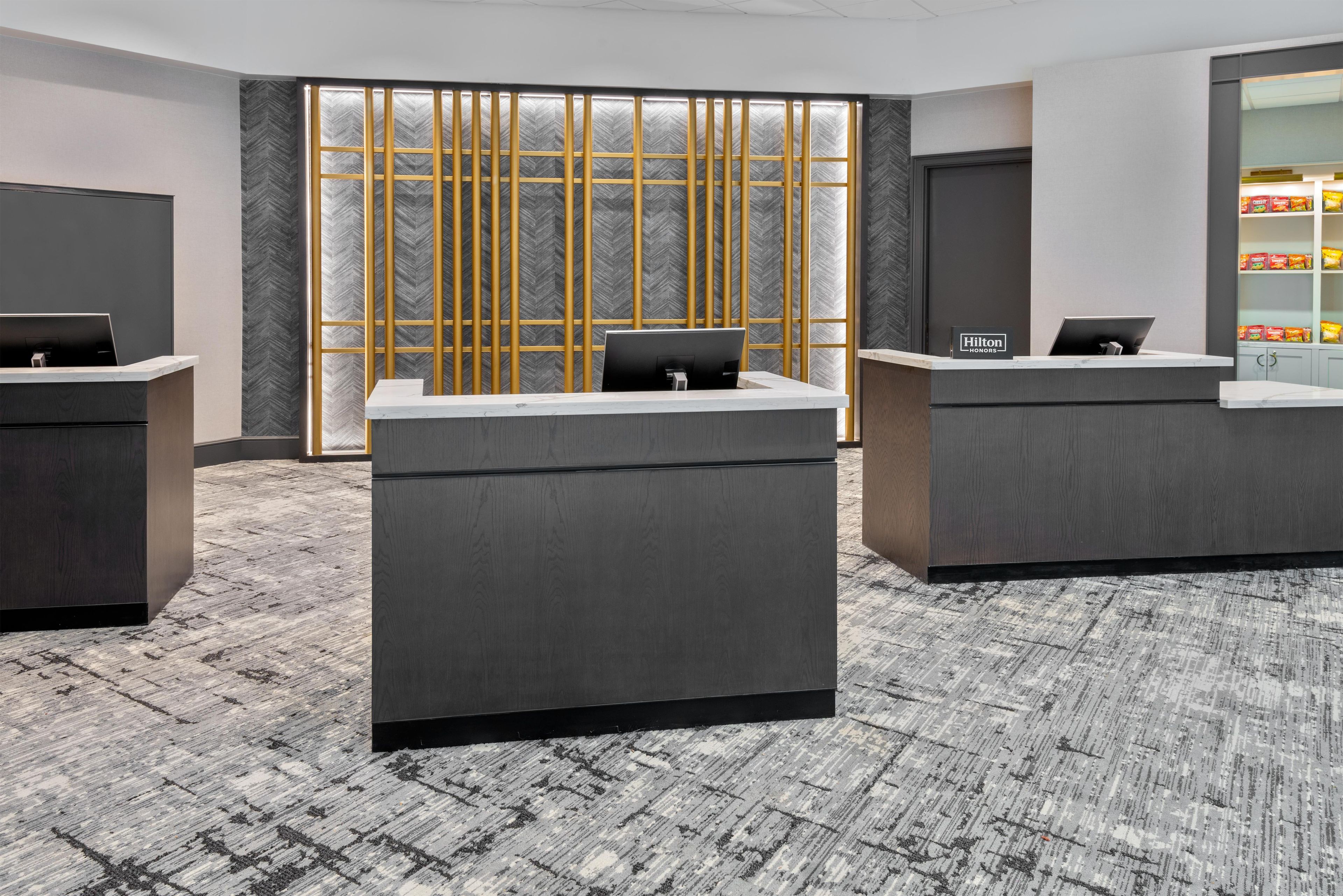 A reception area with three desks, a large window with a herringbone pattern, and a minibar with snacks.