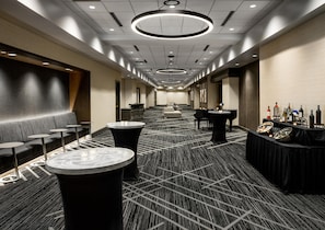 Un couloir d’hôtel aménagé avec des espaces de détente, des tables rondes et un bar.