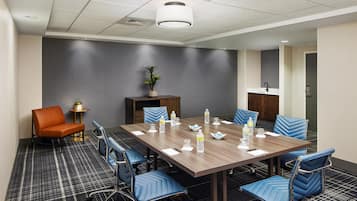 A conference room with a long table, blue chairs, a potted plant, and water bottles.