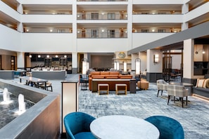 Un hall d’hôtel spacieux comprenant un bar, des espaces de détente et une fontaine décorative.