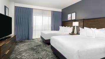 Une chambre d’hôtel avec deux lits, une télévision, un bureau et une fenêtre avec des rideaux.