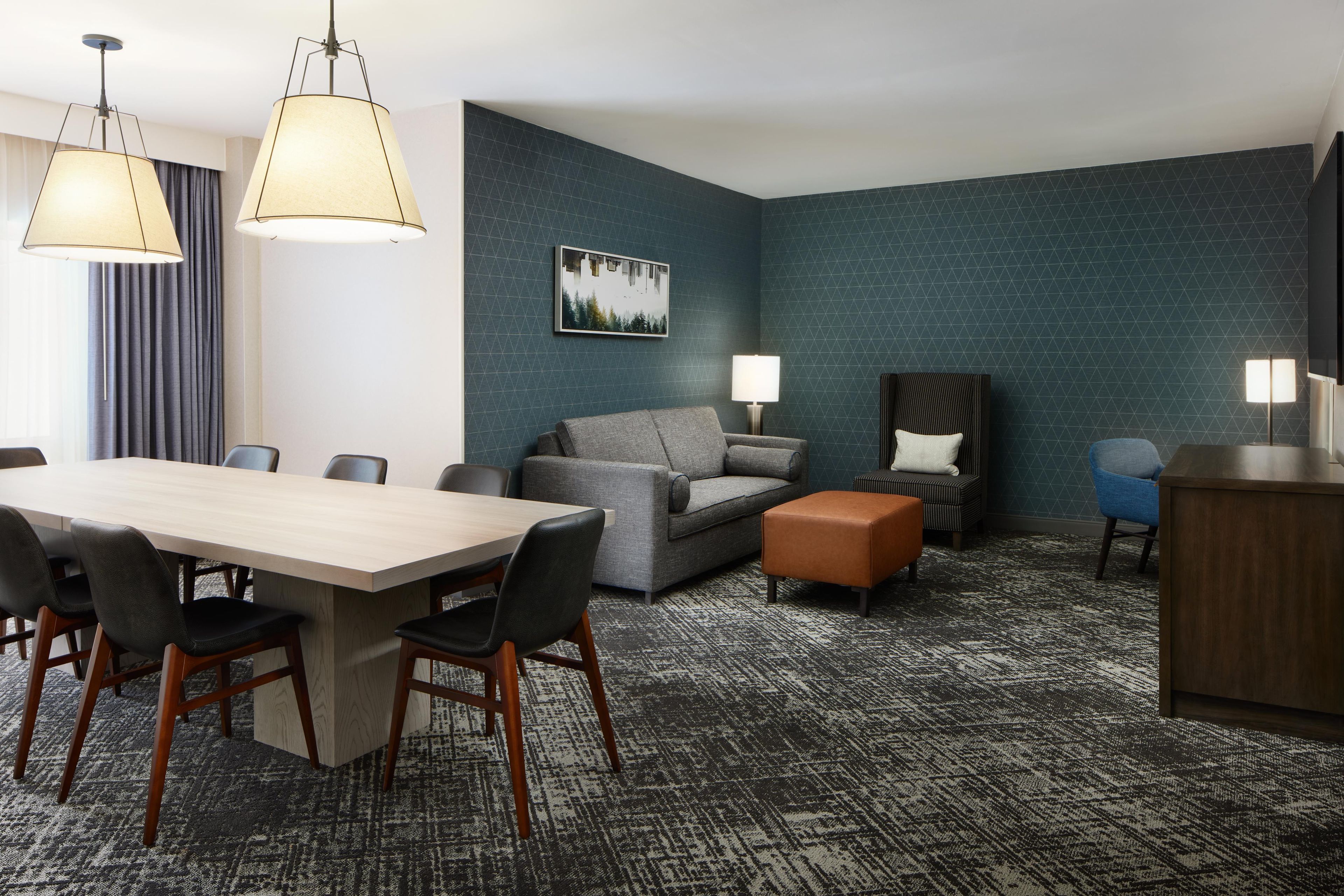 A hotel room with a dining table, chairs, a sofa, a loveseat, a small ottoman, a chair, and a cabinet.