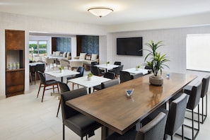 A modern dining area with a long wooden table, multiple chairs, and a television mounted on the wall.